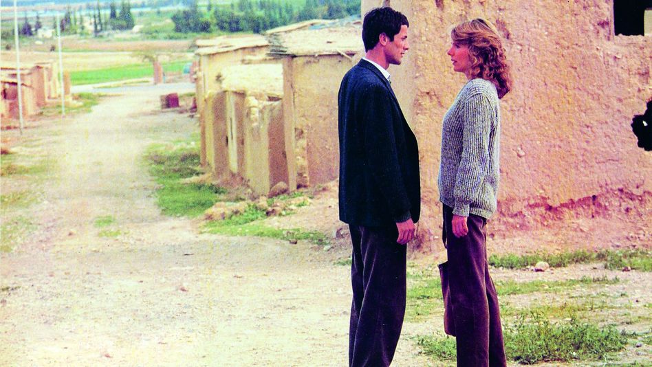 Film still from HANNA K.: A man and a woman stand at the edge of a modest settlement and look at each other.