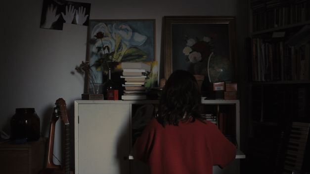 Filmstill aus dem Film "Mun Koti" von Azar Saiyar. Man sieht eine Frau von hinten an einem Sekretär sitzen.