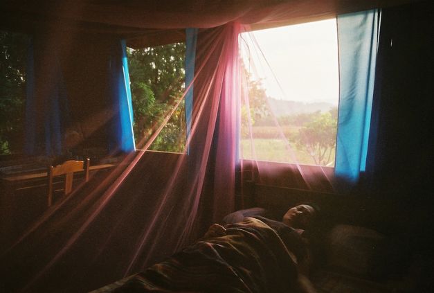 Filmstill aus UNCLE BOONMEE ERINNERT SICH AN SEINE FRÜHEREN LEBEN: Eine Frau liegt direkt am Fenster im Bett. Es sind transparente Vorhänge in verschiedenen Farben aufgehängt. 