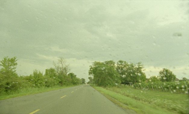 Filmstill aus „Akyn (Poet)“ von Darezhan Omirbayev. Eine leere Straße gesehen aus der Windschutzscheibe eines Autos heraus. 