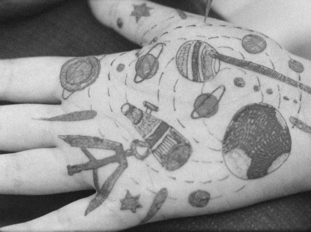 Film still from Gavati Wad’s film “O Seeker”. The palm of a hand with various illustrations drawn onto it, including planets, stars, and lines. 