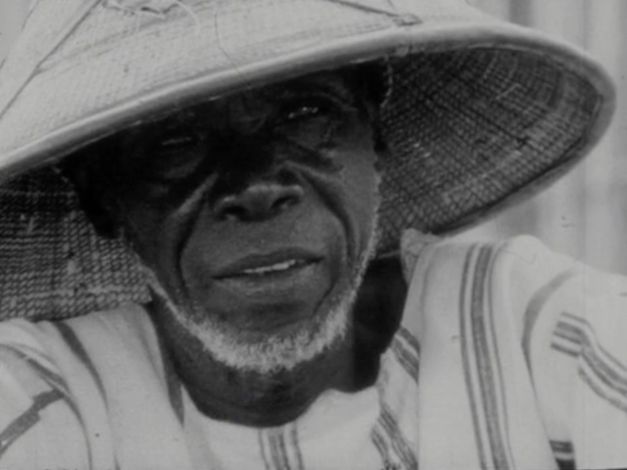 Film still from "Kaddu Beykat" by Safi Faye. It shows a close-up of a man wearing a bamboo hat. 