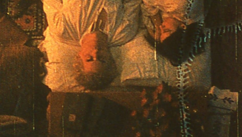 Film still from TO LAVOISIER, WHO DIED IN THE REIGN OF TERROR: Top view of a couple lying in bed. The film material has clearly been altered and shows streaks and stains.