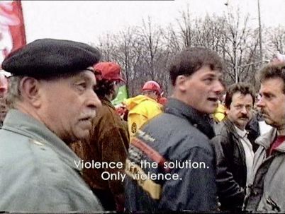 Filmstill aus „Die leere Mitte“ von Hito Steyerl. Menschen auf einer Demonstration. Untertitel: Gewalt ist die Lösung. Nur Gewalt. 