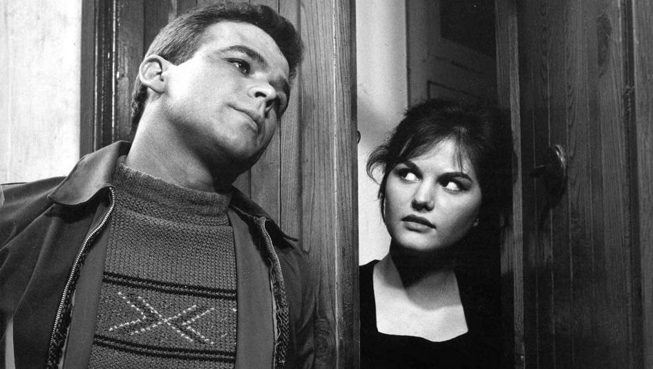 Film still from I SOLITI IGNOTI: A young man and a young woman are leaning against a door frame, she is looking at him sideways.