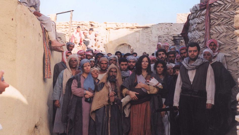 Film still from THE GATE OF SUN: A group of people stand crowded together in an alleyway between houses, gazing into the distance.