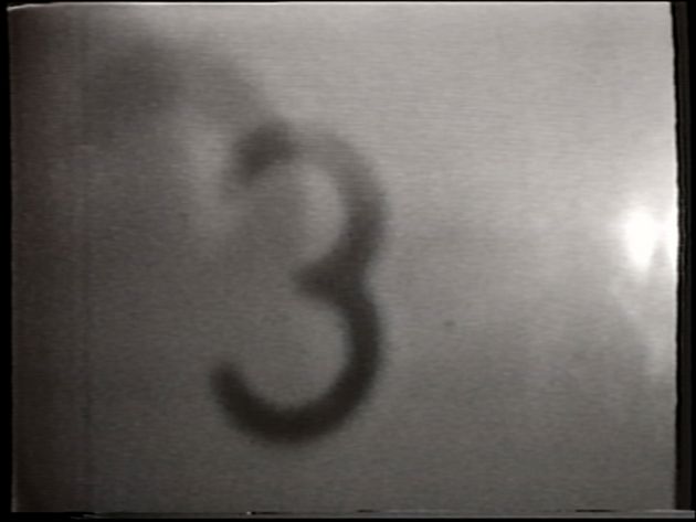 Still aus „Time Tunnel“ von Takahiko Iimura: in schwarz-weiß ist eine Drei zu sehen: die Aufzeichnung der Projektion eines analogen Film-Countdowns 