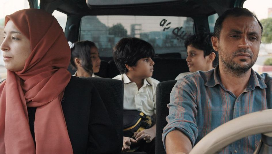Film still from THE BURDENED: A couple in a car with three children in the back seat.