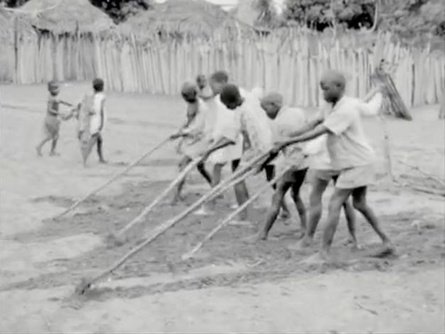 Film still from "Kaddu Beykat" by Safi Faye. It shows six children raking the floor. Two more children are walking in the background. 