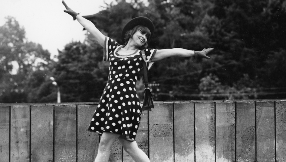 Film still from COMMOTION: A woman in a polka-dot dress dances across the street.