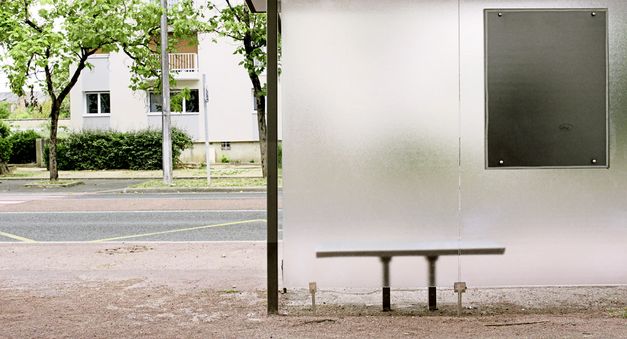 Filmstill aus "Europe" von Philipp Scheffner. Eine menschenleere Bushaltestelle vor einer Straße. 