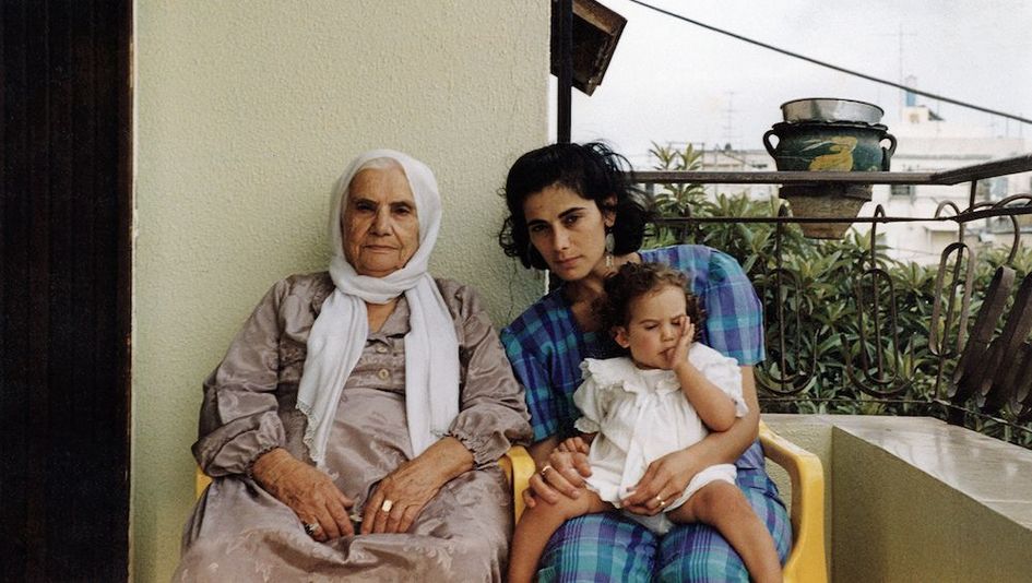 Filmstill aus BYE BYE TIBERIAS: Eine alte und eine junge Frau sitzen nebeneinander auf einem Balkon. Die jüngere Frau hat ein kleines Mädchen auf dem Schoß.