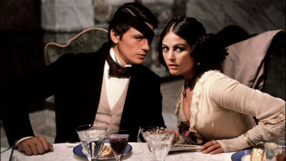 Filmstill aus IL GATTOPARDO: Ein elegant gekleidetes Paar sitzt an einem feierlich gedeckten Tisch.
