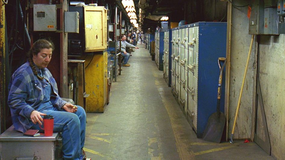 Film still from LUNCH BREAK: A long corridor in a factory. People sit individually in alcoves having lunch.