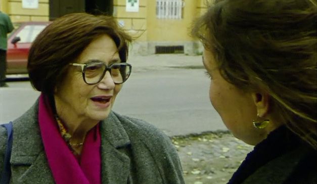 Film still from "Diese Tage in Terezín" by Sibylle Schönemann. It shows a close-up of two women talking on the side of the road. 