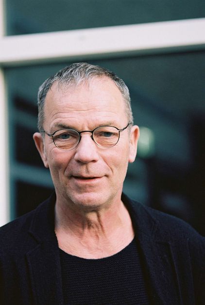 Portrait von Thomas Heise: Ein Mann mit kurzen grauen Haaren, einer Brille mit schmalem Rand. Er lächelt.