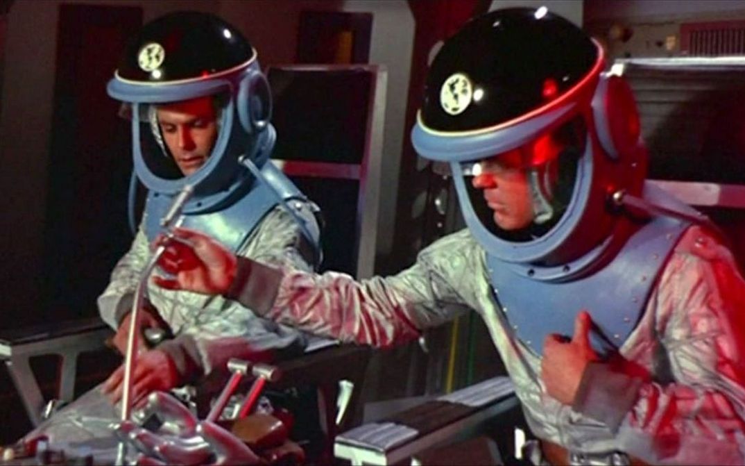 Film still from DER HIMMEL RUFT: Two astronauts with spacesuits in a spaceship.