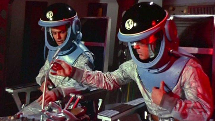 Film still from DER HIMMEL RUFT: Two astronauts with spacesuits in a spaceship.