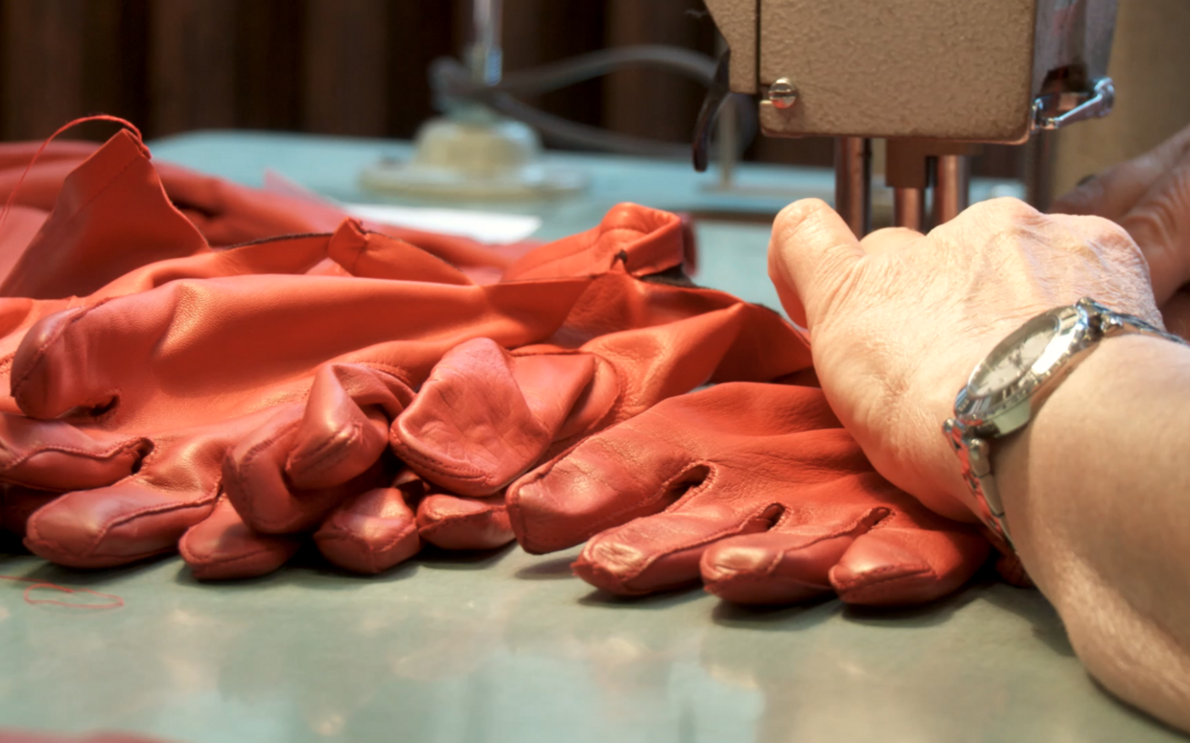 Film still from THE UNSTABLE OBJECT: Red leather gloves are sewn on a sewing machine.