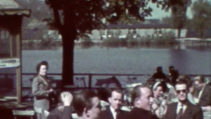 Menschen, die in einem Biergarten sitzen. Im Hintergrund Wasser, die Sonne scheint.