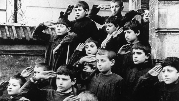Film still from ZÉRO DE CONDUITE: A group of children in front of a building. They are all holding their right hand to their temple.