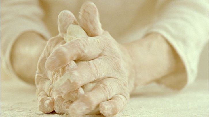 Filmstill aus CUM PANE. Großaufnahme von zwei Händen, die Teig kneten.