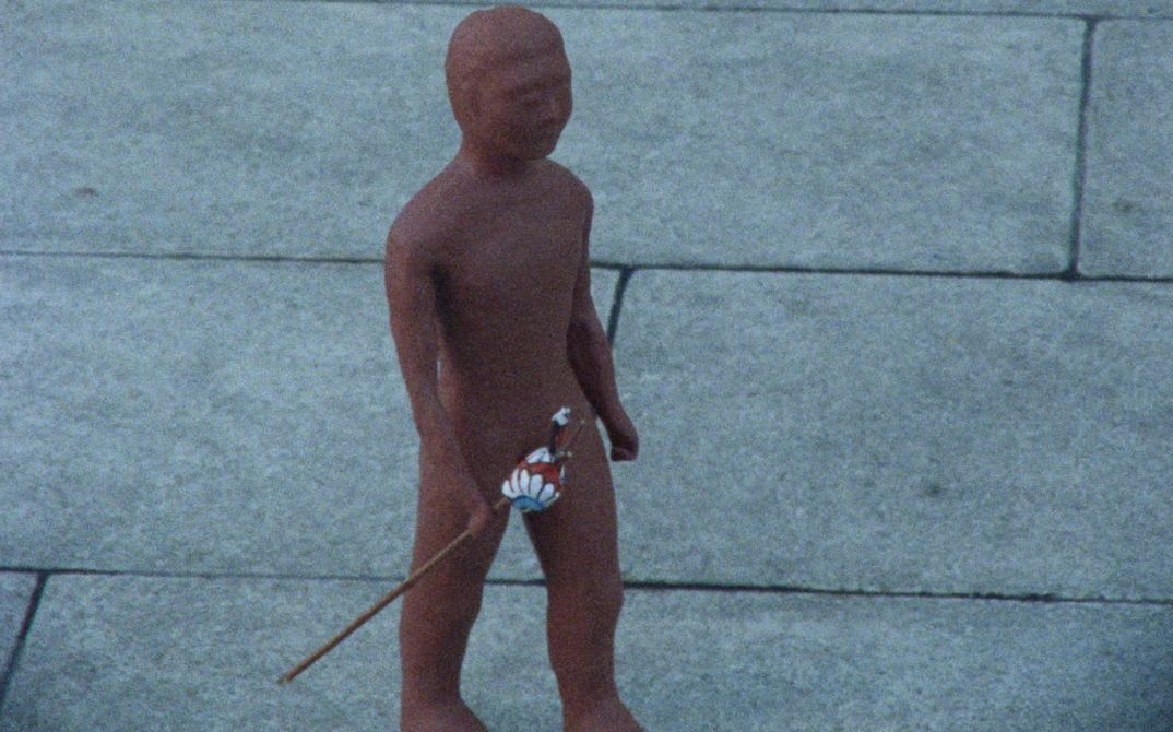 Filmstill aus dem Film "Jordmannen/The Earthmen": eine Tonfigur auf Marmorplatten draußen. 