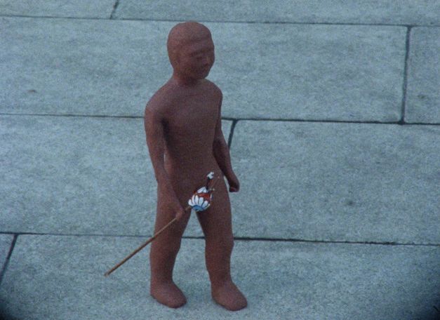 Filmstill aus dem Film "Jordmannen/The Earthmen": eine Tonfigur auf Marmorplatten draußen. 