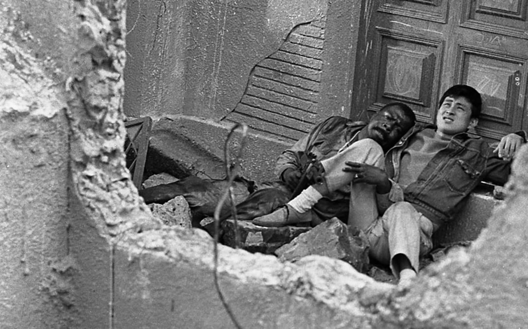 Filmstill aus BLACK SUN: Zwei Männer, einer davon Japaner, der andere ein afroamerikanischer Soldat, sitzen in einem ausgebombten Haus.