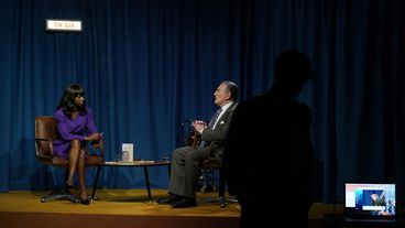 Ein Mann und eine Frau sitzen an einem Tisch wie in einer Talkshow