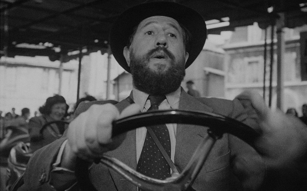 Filmstill aus PANIQUE: Ein Mann in Anzug und Hut fährt alleine Autoscooter.