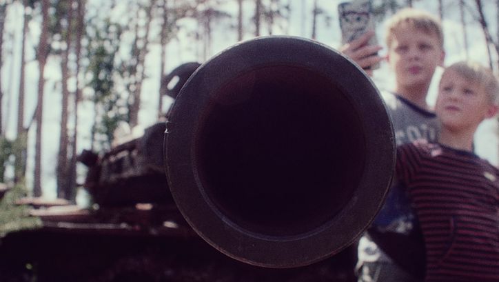 Ein Panzerrohr ist auf die Kamera gerichtet und scharf im Vordergrund, dahinter sind im unschwarfen Bereich zwei Kinder zu sehen, die mit einem Handy ein Foto davon machen.