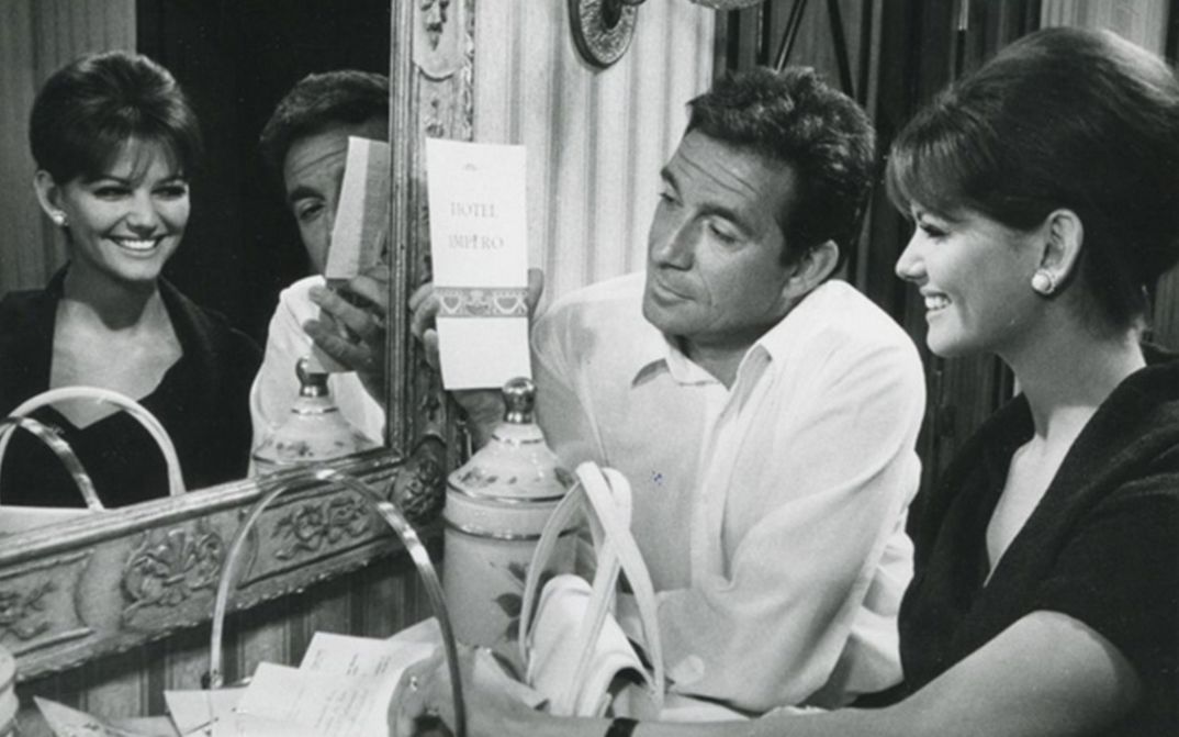 Filmstill aus IL MAGNIFICO CORNUTO: Eine Frau und ein Mann sitzen lachend vor einem Spiegel.