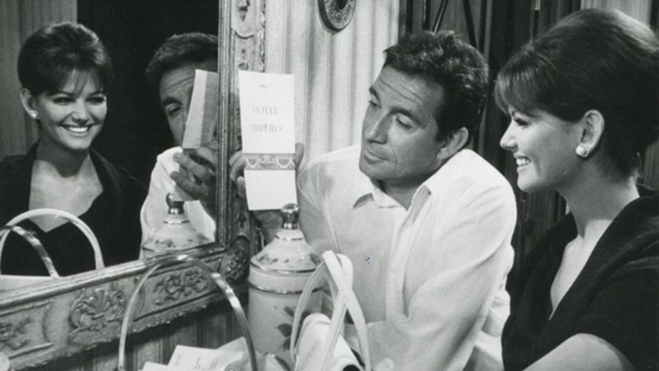 Film still from IL MAGNIFICO CORNUTO: A woman and a man sit laughing in front of a mirror.