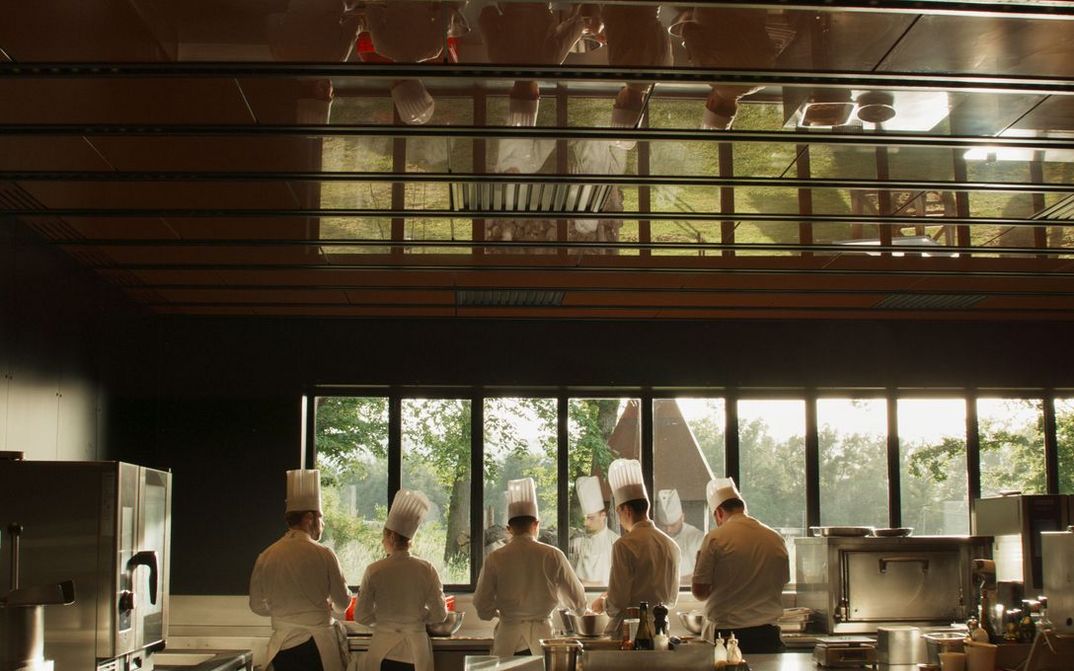 Filmstill aus MENUS PLAISIRS: Fünf Köche stehen nebeneinander in der Küche. Durch eine Spiegelung sind sie doppelt zu sehen.