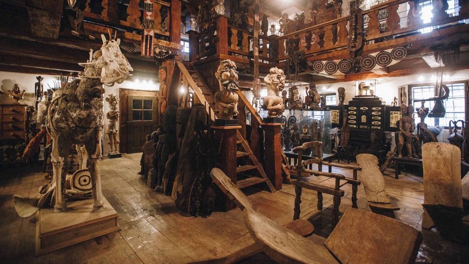 Film still from KUNSTKAMERA by Jan Švankmajer : A large room with stairs leading to a gallery on the upper floor. The room is filled with art historical artifacts, many of them made of wood.