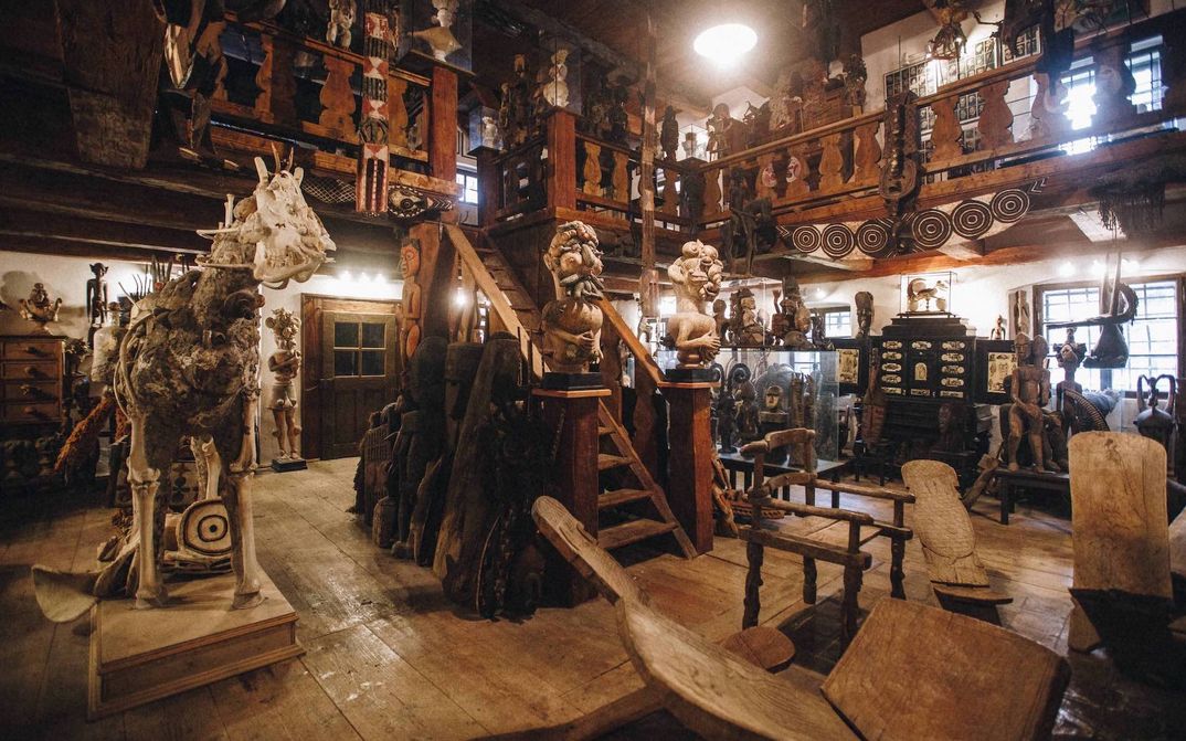 Filmstill aus KUNSTKAMERA von Jan Švankmajer : Ein großer Raum mit Treppe in eine Galerie im Obergeschoß. Der Raum ist voller kunsthistorischer Artefakte, viele davon aus Holz.
