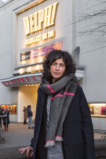 Eine Frau steht draußen vor dem Kino und schaut in die Kamera.