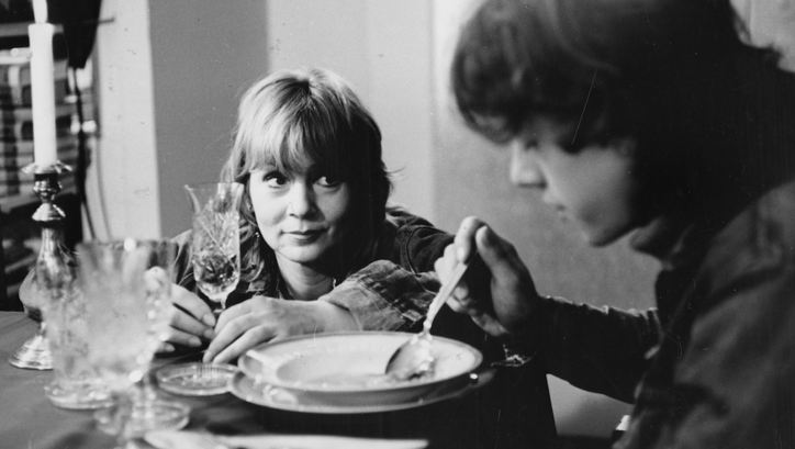 Filmstill aus DIE BEUNRUHIGUNG: Eine Frau sitzt am Tisch und blickt ihren Sohn an, der eine Suppe isst. 