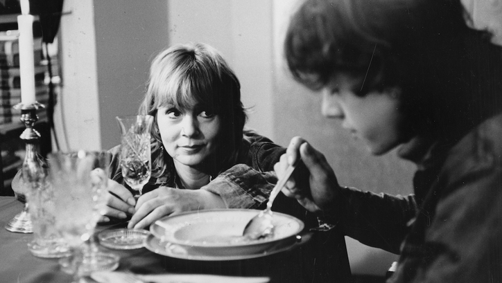 Filmstill aus DIE BEUNRUHIGUNG: Eine Frau sitzt am Tisch und blickt ihren Sohn an, der eine Suppe isst. 