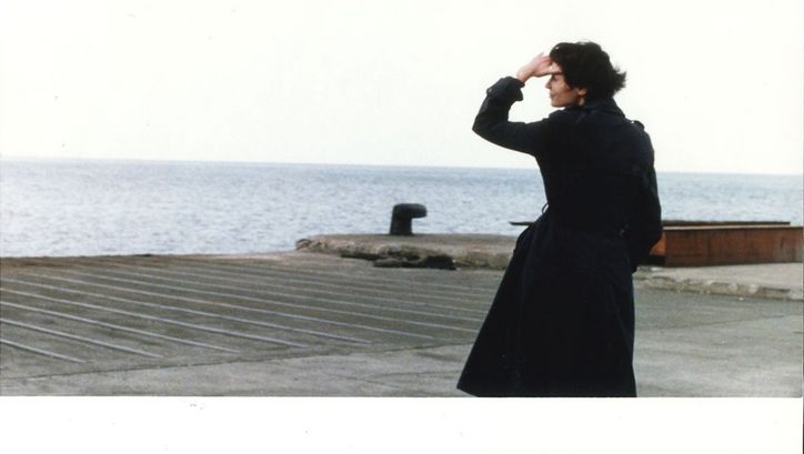 Filmstill aus LE STADE DE WIMBLEDON. Eine Frau in einem dunklen Mantel blickt aufs Meer.