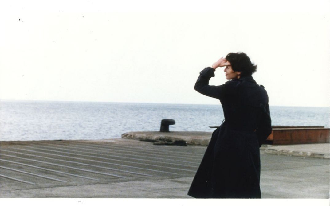 Filmstill aus LE STADE DE WIMBLEDON. Eine Frau in einem dunklen Mantel blickt aufs Meer.