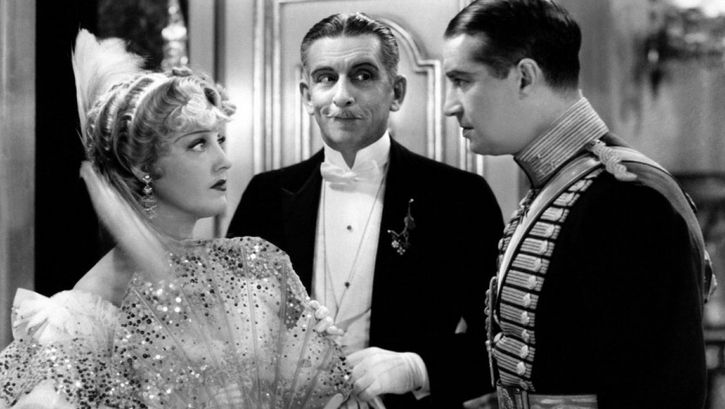 Film still from THE MERRY WIDOW: A young woman and a young man, both festively dressed, look at each other. An elderly gentleman stands in the background.