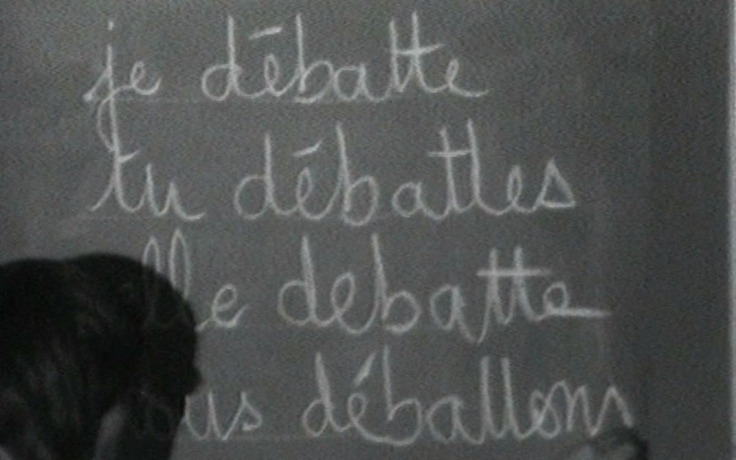 Film still from MUSIDORA: FESTIVAL INTERNATIONAL DES FILMS DE FEMMES: The French verb “débattre” is conjugated on a blackboard.
