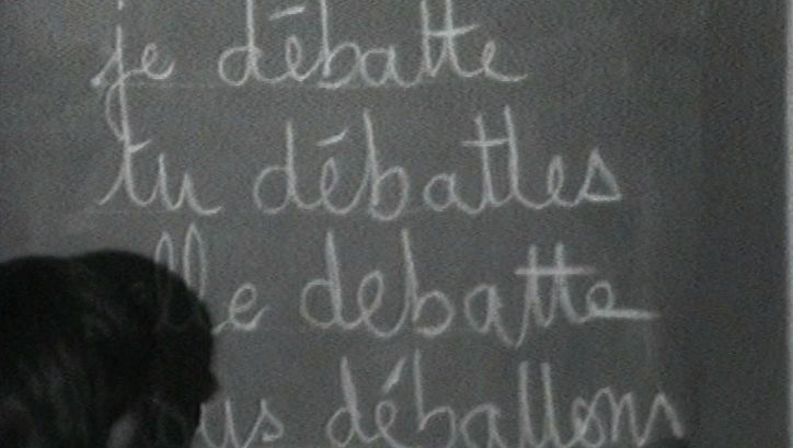 Filmstill aus MUSIDORA: FESTIVAL INTERNATIONAL DES FILMS DE FEMMES: Auf einer Schultafel steht das französische Wort "débattre" konjugiert.