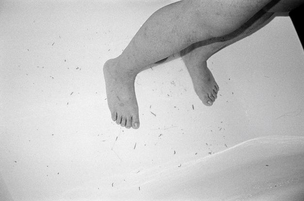 Still from the film "Jet Lag" by Zheng Lu Xinyuan. A black-and-white image of two legs standing against a grey background, photographed looking down. 