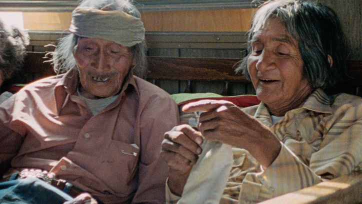 Filmstill aus "Techqua Ikachi, Land – mein Leben" von Anka Schmid, James Danaqyumptewa und Agnes Barmettler. Zu sehen sind ein alter Mann und eine alte Frau, die nebeneinander sitzen. Der Mann hat einen Verband um seinen Kopf. 