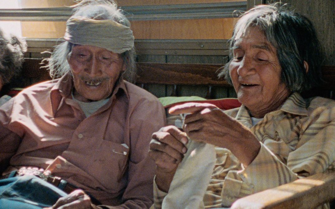 Filmstill aus "Techqua Ikachi, Land – mein Leben" von Anka Schmid, James Danaqyumptewa und Agnes Barmettler. Zu sehen sind ein alter Mann und eine alte Frau, die nebeneinander sitzen. Der Mann hat einen Verband um seinen Kopf.