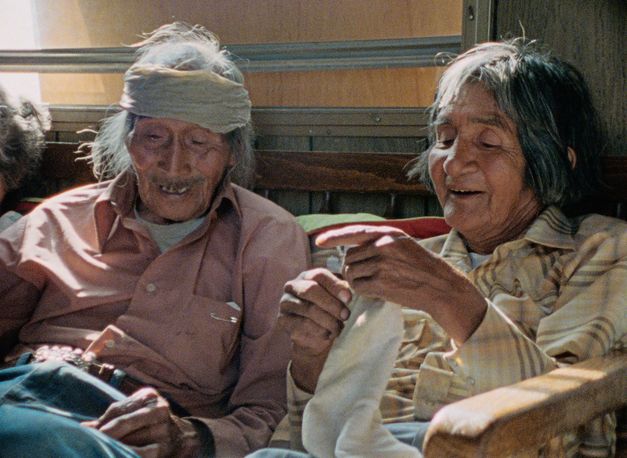 Filmstill aus "Techqua Ikachi, Land – mein Leben" von Anka Schmid, James Danaqyumptewa und Agnes Barmettler. Zu sehen sind ein alter Mann und eine alte Frau, die nebeneinander sitzen. Der Mann hat einen Verband um seinen Kopf. 