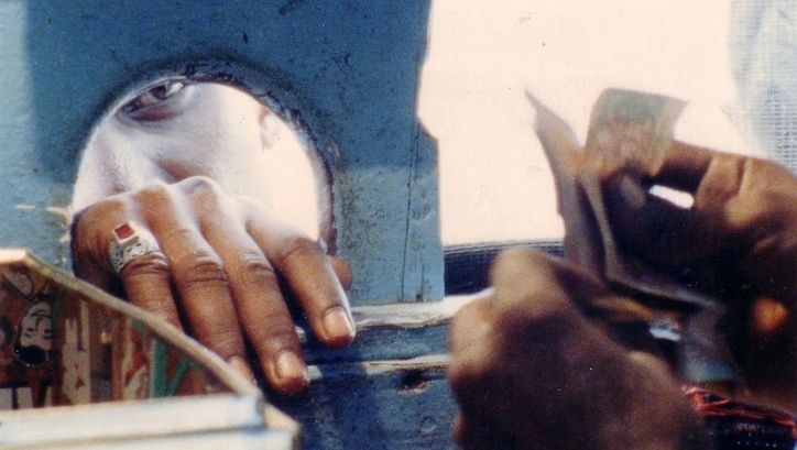Filmstill aus KUMAR TALKIES: Aus dem Inneren eines Kassenhauses. Von außen sieht man das Gesicht einer Person, die soeben Geld hineingereicht hat.